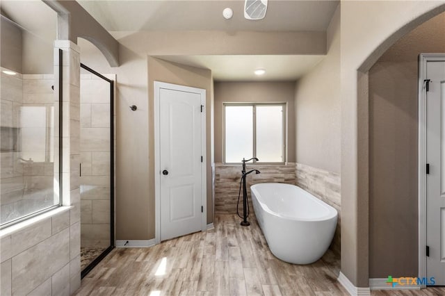 bathroom featuring a stall shower, a wainscoted wall, wood finished floors, a freestanding bath, and tile walls