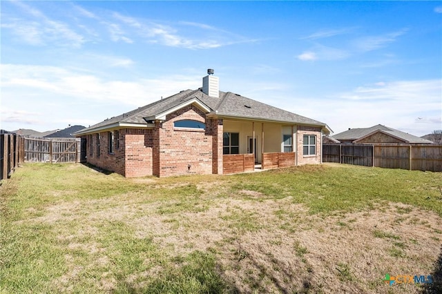 rear view of house with a fenced backyard, a chimney, a lawn, and brick siding