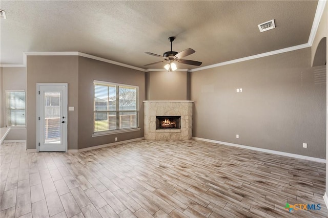 unfurnished living room with a textured ceiling, a fireplace, visible vents, light wood finished floors, and crown molding