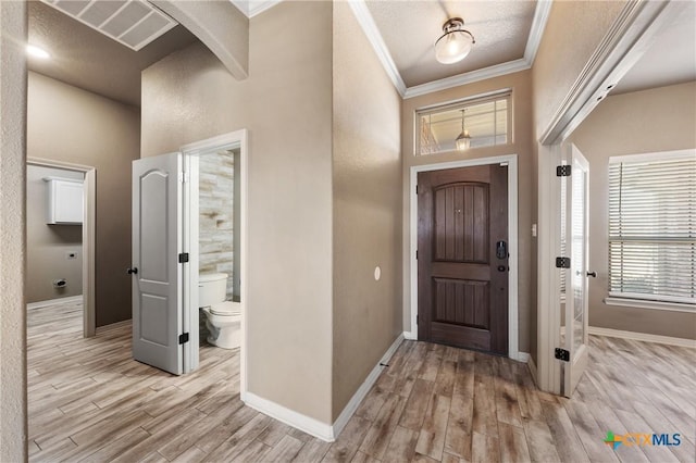 foyer entrance with light wood-type flooring, crown molding, arched walkways, and baseboards