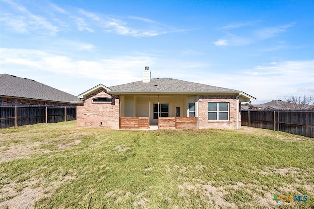 rear view of house featuring a fenced backyard, a chimney, a lawn, and brick siding