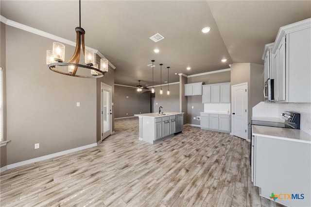 kitchen featuring light countertops, hanging light fixtures, stainless steel microwave, decorative backsplash, and an island with sink