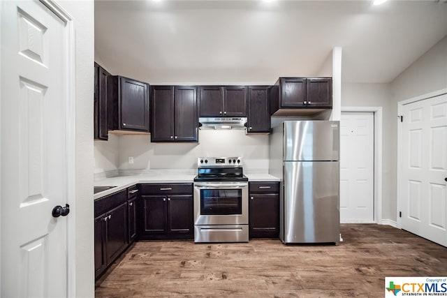 kitchen with appliances with stainless steel finishes, dark brown cabinets, and light hardwood / wood-style floors