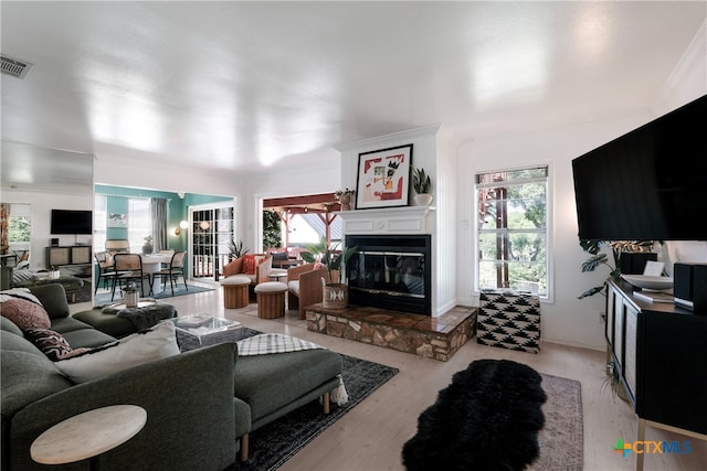 living area featuring a glass covered fireplace, light wood finished floors, and visible vents