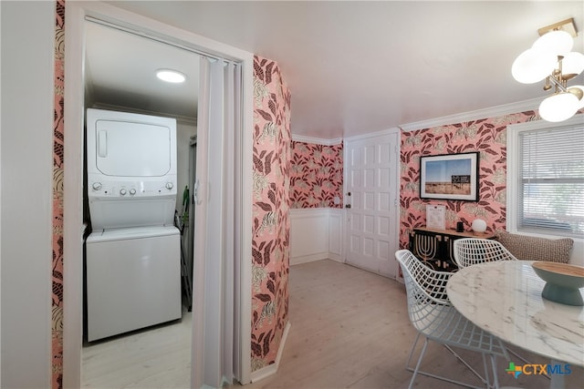 laundry area featuring laundry area, stacked washer / dryer, wood finished floors, a wainscoted wall, and wallpapered walls