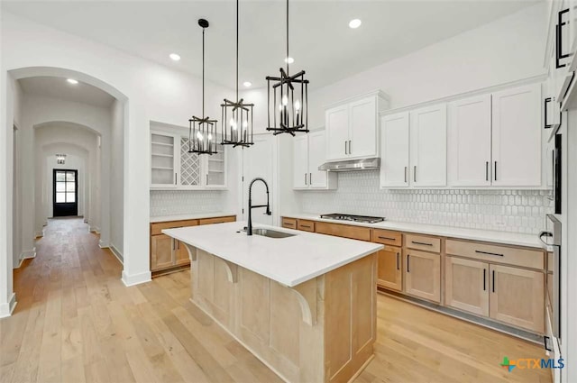 kitchen with stainless steel gas cooktop, sink, white cabinetry, decorative light fixtures, and a center island with sink