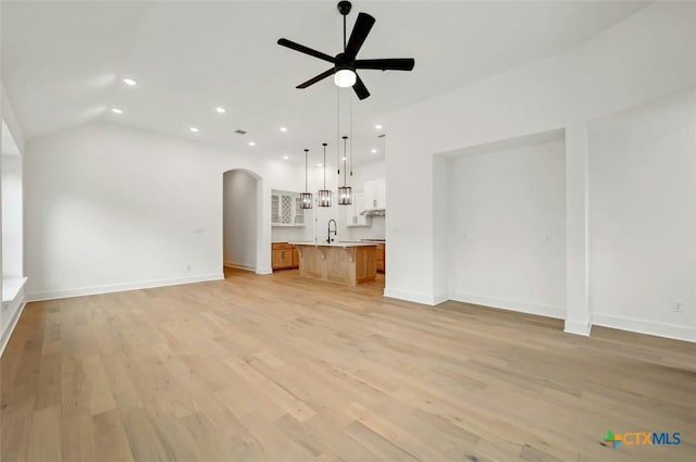 unfurnished living room with vaulted ceiling, sink, ceiling fan, and light hardwood / wood-style flooring