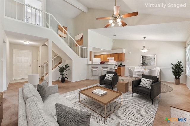 living room with beamed ceiling, light colored carpet, stairs, high vaulted ceiling, and a ceiling fan