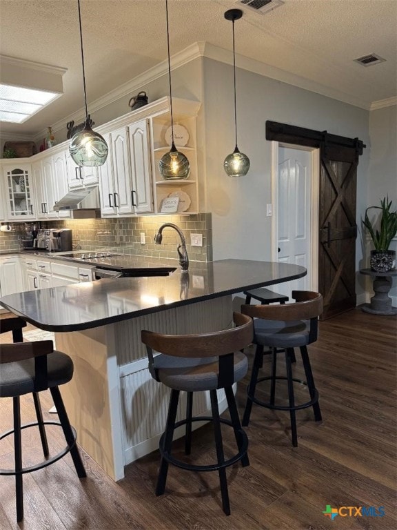 507 Hackberry Bnd, Port Lavaca, TX 77979 - kitchen featuring dark wood-style flooring, a barn door, tasteful backsplash, white cabinetry, and crown molding