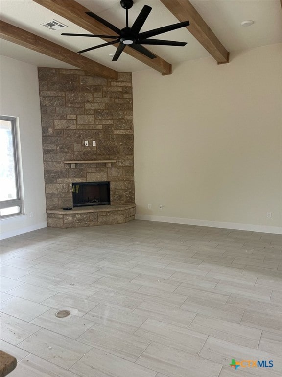 unfurnished living room featuring beam ceiling, a stone fireplace, and ceiling fan