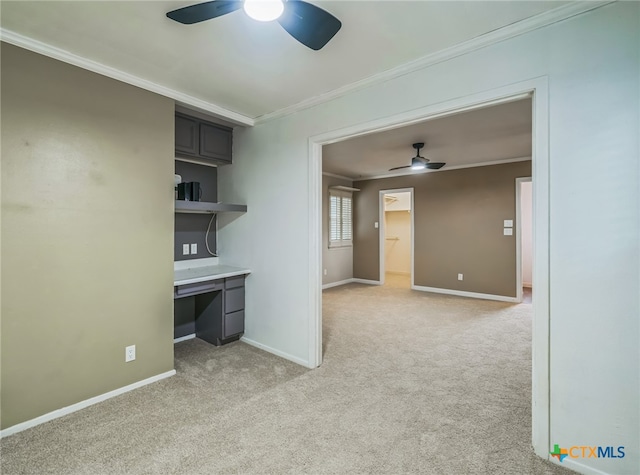 carpeted spare room featuring ceiling fan, built in desk, and ornamental molding