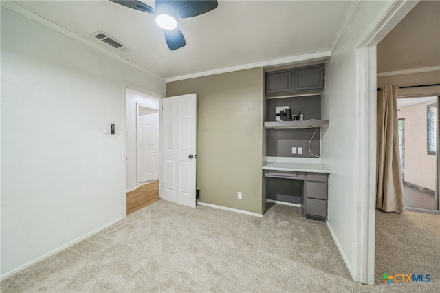 unfurnished office featuring built in desk, light colored carpet, ceiling fan, and crown molding