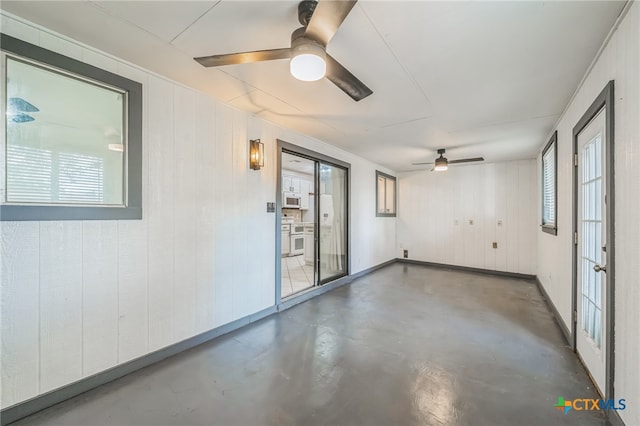 empty room with wood walls, ceiling fan, and concrete floors