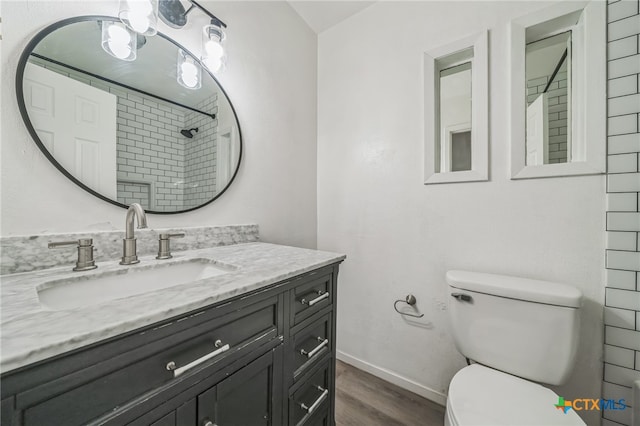 bathroom featuring tiled shower, wood-type flooring, toilet, and vanity