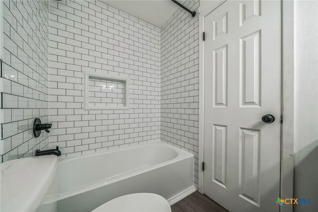 bathroom with hardwood / wood-style flooring, tiled shower / bath, and toilet