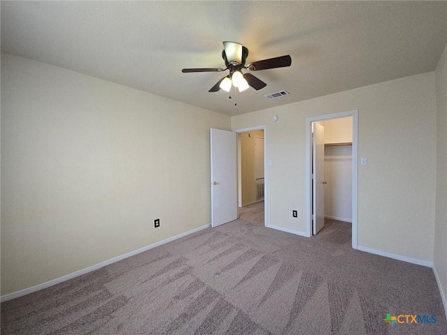 unfurnished bedroom with a walk in closet, light colored carpet, visible vents, a ceiling fan, and baseboards