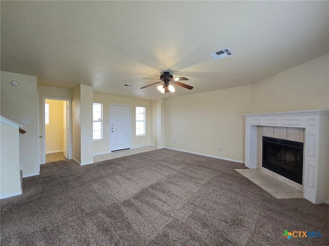 unfurnished living room with a tile fireplace, light carpet, visible vents, baseboards, and stairway