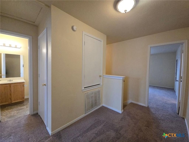 hallway featuring visible vents, baseboards, carpet, an upstairs landing, and a sink