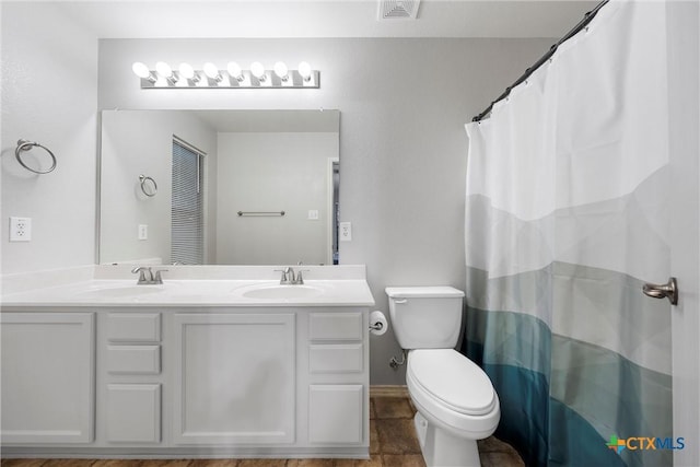 full bath with visible vents, a sink, double vanity, and toilet