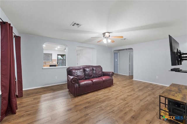 living room with visible vents, wood finished floors, baseboards, ceiling fan, and arched walkways