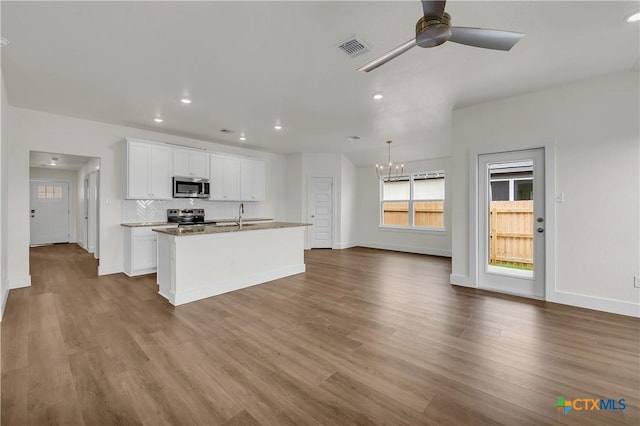 kitchen featuring wood-type flooring, appliances with stainless steel finishes, white cabinetry, and an island with sink