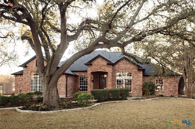 view of front of home featuring a front yard, brick siding, and roof with shingles