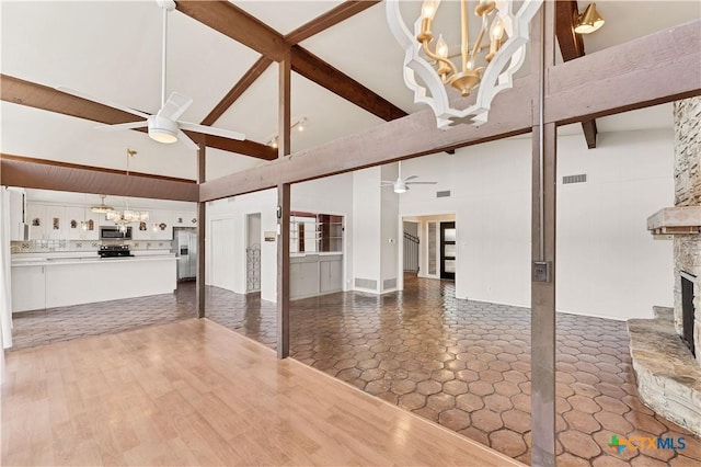 667 Fredericksburg Rd, New Braunfels, TX 78130 - unfurnished living room featuring visible vents, beam ceiling, dark wood-type flooring, ceiling fan with notable chandelier, and a stone fireplace