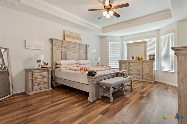 bedroom with dark hardwood / wood-style flooring, a tray ceiling, multiple windows, and ceiling fan