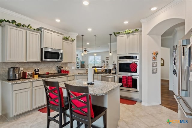 kitchen featuring crown molding, appliances with stainless steel finishes, a kitchen bar, pendant lighting, and kitchen peninsula