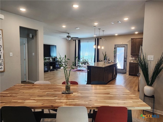 interior space with sink, a kitchen island with sink, dark brown cabinetry, decorative light fixtures, and light wood-type flooring