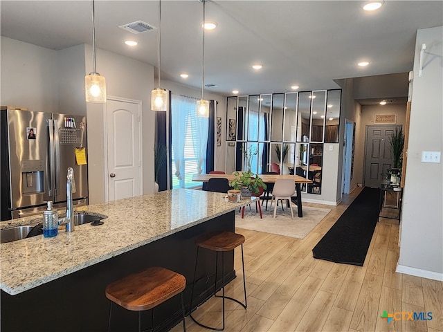 kitchen with light stone countertops, stainless steel fridge with ice dispenser, light hardwood / wood-style flooring, and hanging light fixtures