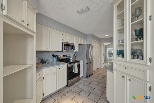 kitchen featuring white cabinetry, light tile patterned floors, stainless steel appliances, and a textured ceiling