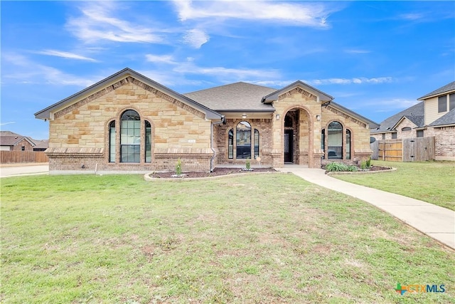 view of front facade featuring roof with shingles, fence, a front lawn, and brick siding