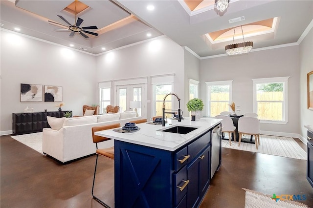 kitchen with ceiling fan with notable chandelier, blue cabinets, sink, a kitchen island with sink, and a tray ceiling