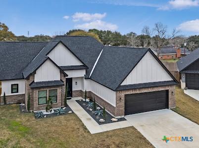 modern farmhouse with a garage, brick siding, a shingled roof, driveway, and board and batten siding