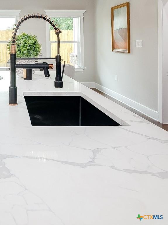 kitchen view of a sink, baseboards, and light stone countertops