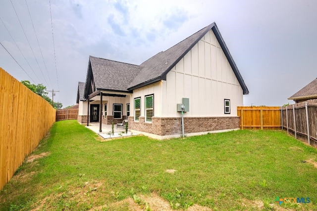 rear view of house with board and batten siding, a shingled roof, a patio area, and brick siding