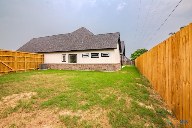 back of house with a shingled roof, central air condition unit, brick siding, and board and batten siding