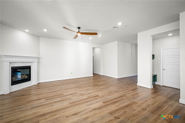 unfurnished living room with ceiling fan, a textured ceiling, and light hardwood / wood-style flooring