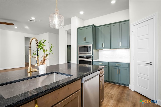 kitchen featuring tasteful backsplash, sink, hanging light fixtures, appliances with stainless steel finishes, and dark stone counters