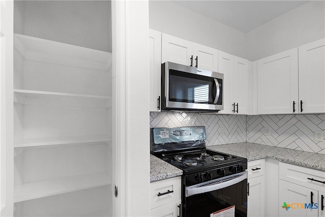 kitchen featuring tasteful backsplash, light stone countertops, white cabinets, and black range oven