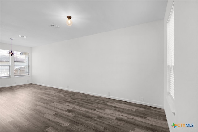 empty room with a notable chandelier and dark hardwood / wood-style floors