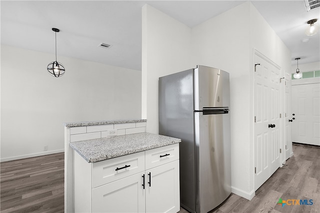 kitchen with wood-type flooring, light stone counters, stainless steel refrigerator, hanging light fixtures, and white cabinets