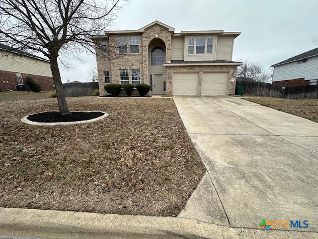 traditional-style house featuring brick siding, fence, driveway, and an attached garage