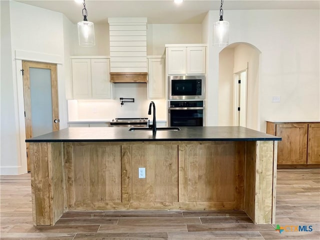 2819 Isaac Cir, Belton, TX 76513 - kitchen with stainless steel appliances, a sink, arched walkways, light wood-style floors, and dark countertops