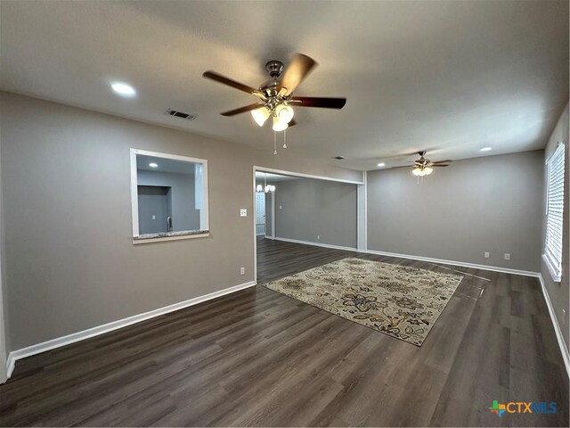 spare room featuring ceiling fan with notable chandelier and dark wood-type flooring