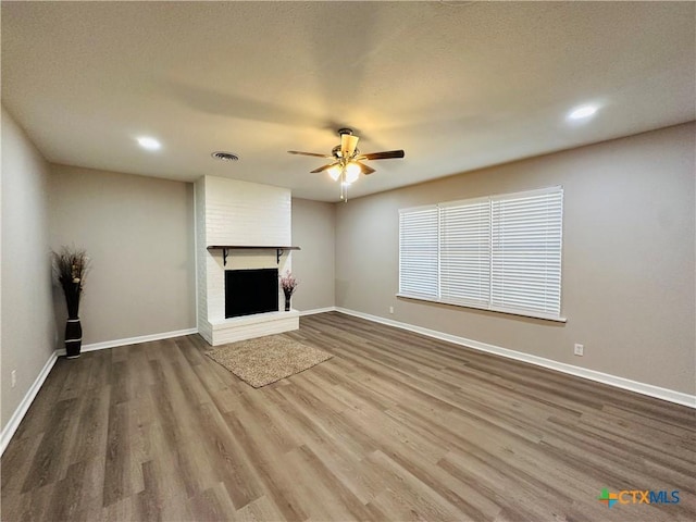 unfurnished living room featuring a brick fireplace, wood-type flooring, and ceiling fan