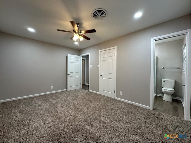 unfurnished bedroom featuring ceiling fan, dark colored carpet, and ensuite bath