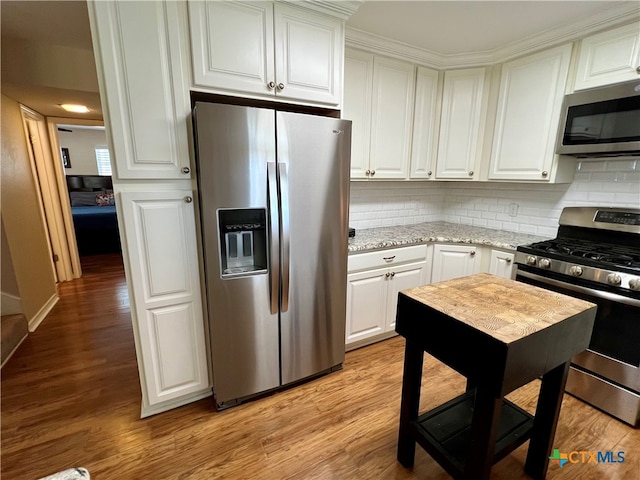 kitchen with light stone countertops, white cabinetry, stainless steel appliances, decorative backsplash, and light wood-type flooring