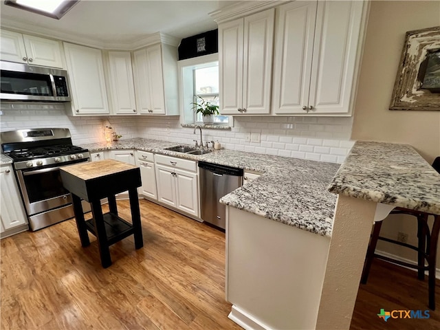 kitchen with white cabinetry, kitchen peninsula, stainless steel appliances, a breakfast bar, and sink